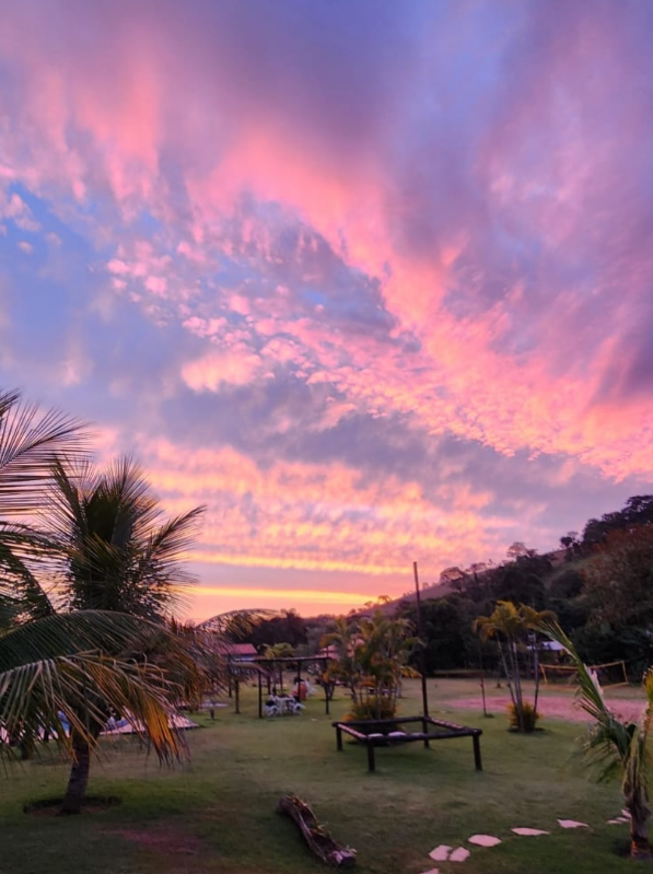 Pôr do sol em tons de rosa sobre o jardim da pousada