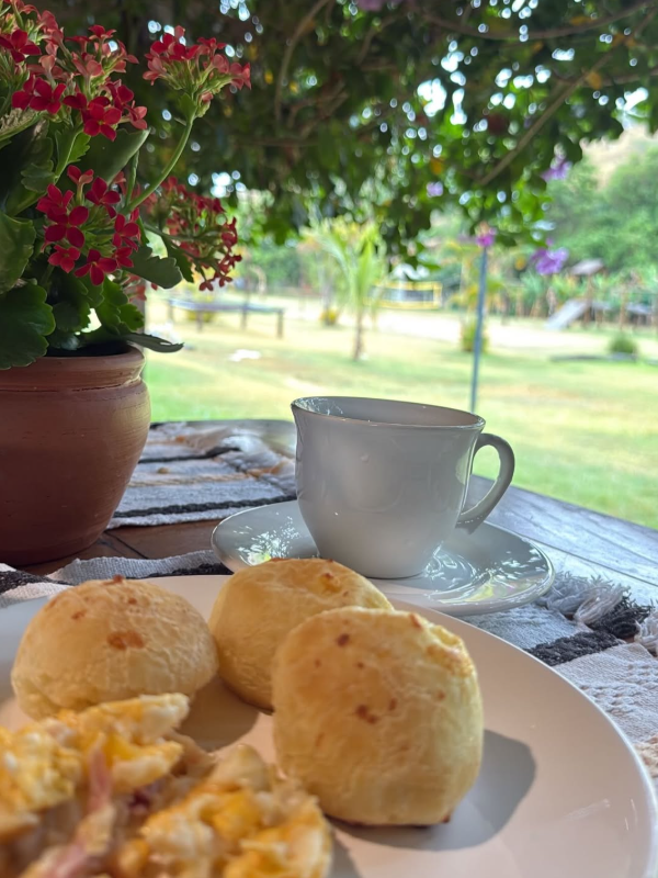 Café e pão de queijo à mesa, com o jardim ao fundo